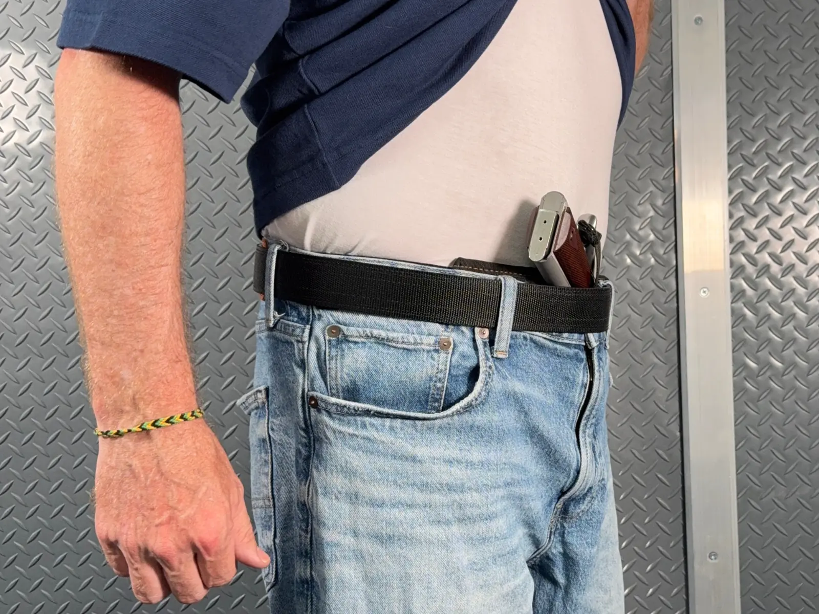 Shirt lifted showing a full-size 1911 carried in the waistband with no pillow, grip leaning away from the body